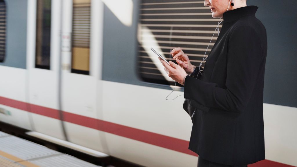 Kobieta stojąca na peronie i spoglądająca w telefon komórkowy